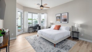 A modern bedroom with a bed, desk, and chair, a ceiling fan, and a view of the outdoors. - Edgemont Escape-  3 King Beds, heated pool*, close to spring training,  (Goodyear)