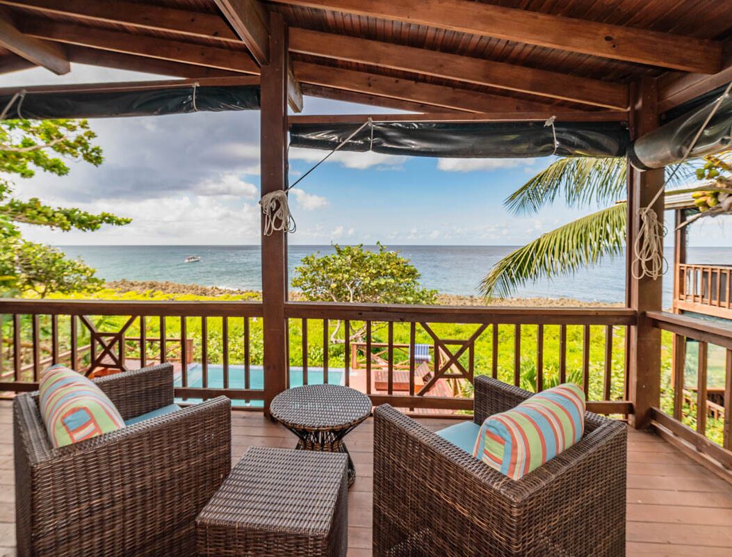 A covered outdoor seating area with wicker furniture and a view of the ocean.