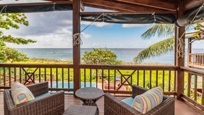 A covered outdoor seating area with wicker furniture and a view of the ocean.