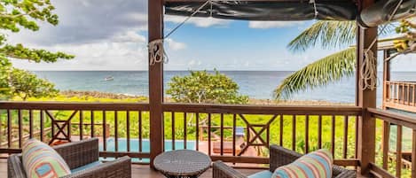 A covered outdoor seating area with wicker furniture and a view of the ocean.