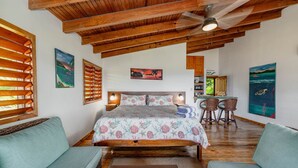 A bedroom with a bed, two nightstands, a ceiling fan, and a dining area with a table and chairs.
