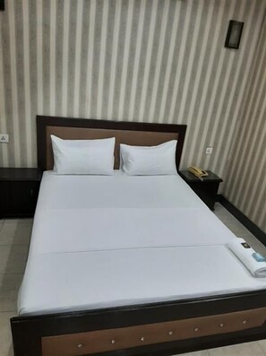 Una cama bien tendida con sábanas blancas en una habitación de hotel con papel tapiz a rayas.
