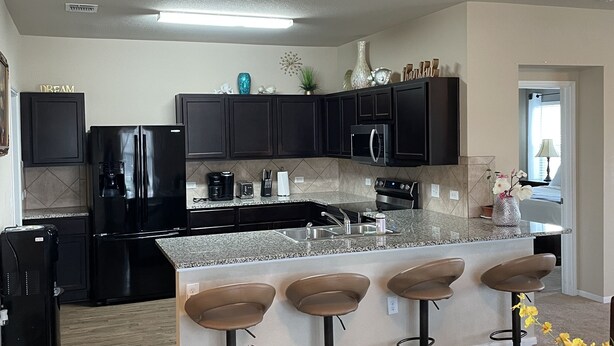 A modern kitchen with dark cabinetry, a granite countertop, and a central island with bar stools. - Single home  with 5 bedrooms  sleep 10 at  a corner lot, fully garage to use (Pflugerville)
