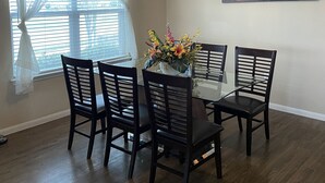 A dining area with a glass table surrounded by chairs, a chandelier, a window with sheer curtains, and a landscape painting on the wall. - Single home  with 5 bedrooms  sleep 10 at  a corner lot, fully garage to use (Pflugerville)