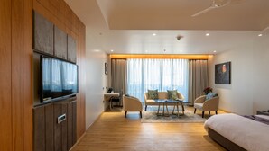 Et moderne hotelværelse med en væg af træpaneler, et fladskærms-tv, en sofa, et spisebord og en stor seng.