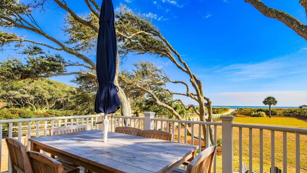 A wooden deck with a table and chairs, overlooking a grassy area and a view of the ocean. - Live Your Best Oceanfront Life!  Exquisite Ocean Views, Private Pool, Expansive Outdoor Areas & More (Isle of Palms)