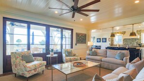 A spacious living room with a large window, a ceiling fan, and a kitchen area with a stone backsplash. - Live Your Best Oceanfront Life!  Exquisite Ocean Views, Private Pool, Expansive Outdoor Areas & More (Isle of Palms)