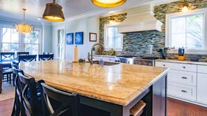 A kitchen with a large island, pendant lighting, a stone backsplash, and a view of the outdoors. - Live Your Best Oceanfront Life!  Exquisite Ocean Views, Private Pool, Expansive Outdoor Areas & More (Isle of Palms)