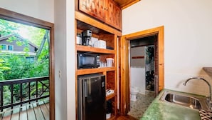 A compact kitchen with a refrigerator, microwave, and sink. A balcony with a railing is visible, and a house can be seen through the window. - Oak Ridge Suite - Ground Level Double (West End)