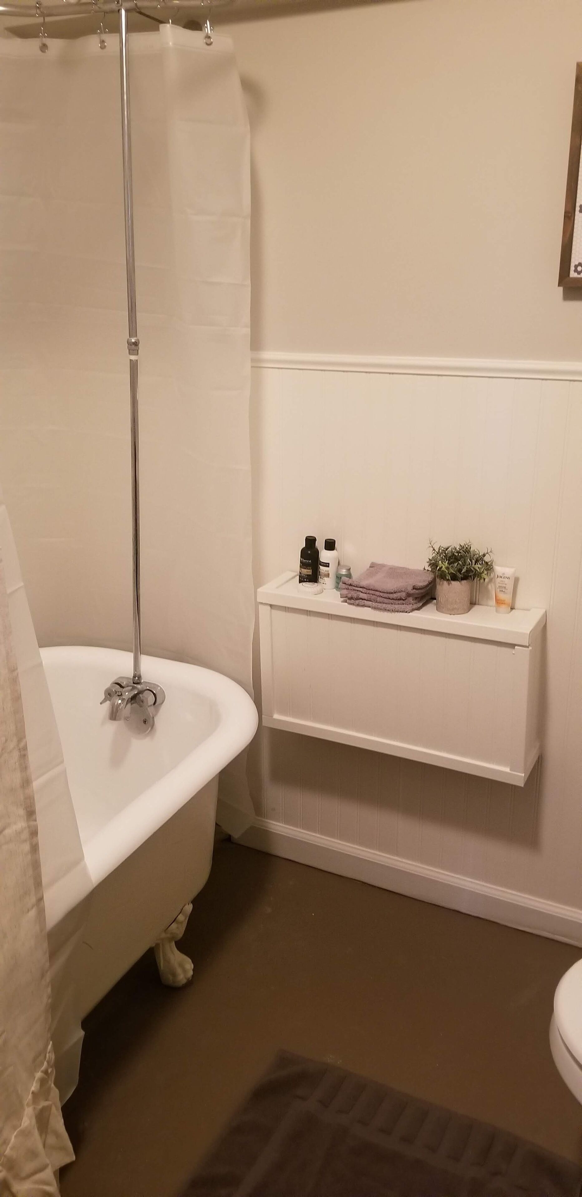 A bathroom with a clawfoot bathtub, a shower curtain, a toilet, and a shelf with toiletries.