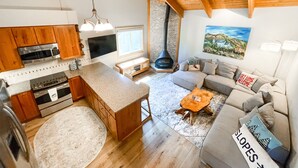 Amplia sala de estar con cocina, vigas de madera en el techo, chimenea y un gran ventanal.
