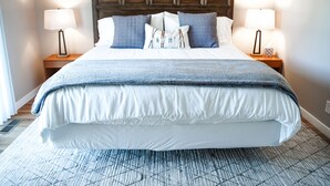 Una cama bien hecha con tablero de madera, dos mesitas de noche con lámparas y una alfombra estampada.