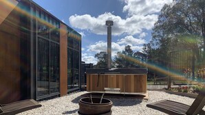 An outdoor seating area with a hot tub, a fire pit, and a modern building with large windows. - 5 star couples hideaway in the country, enjoy privacy and space - w hot tub (Penrose)