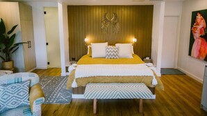 A modern bedroom with a wooden headboard, a large bed with multiple pillows, a bedside table, and a nightstand. There is a potted plant and a patterned rug on the floor. - 5 star couples hideaway in the country, enjoy privacy and space - w hot tub (Penrose)