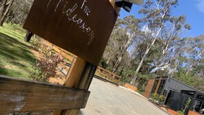 A wooden sign with the text "The Hideaway" in a rustic font, mounted on a post with a camera above it, set against a backdrop of trees and a modern building. - 5 star couples hideaway in the country, enjoy privacy and space - w hot tub (Penrose)
