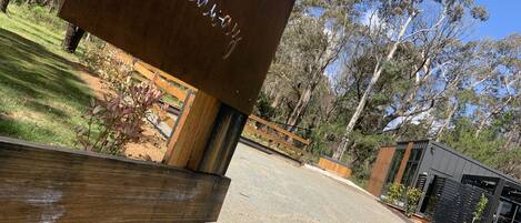 A wooden sign with the text "The Hideaway" in a rustic font, mounted on a post with a camera above it, set against a backdrop of trees and a modern building.