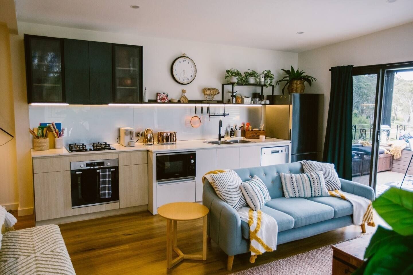 A modern kitchen with integrated appliances, a dining area with a blue sofa, and a view of the outdoors.