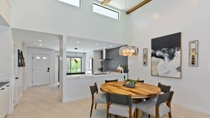 Eine moderne Küche mit einer zentralen Kochinsel, einem Essbereich mit rundem Holztisch und grauen Polsterstühlen sowie einem großen, abstrakten Gemälde an der Wand.