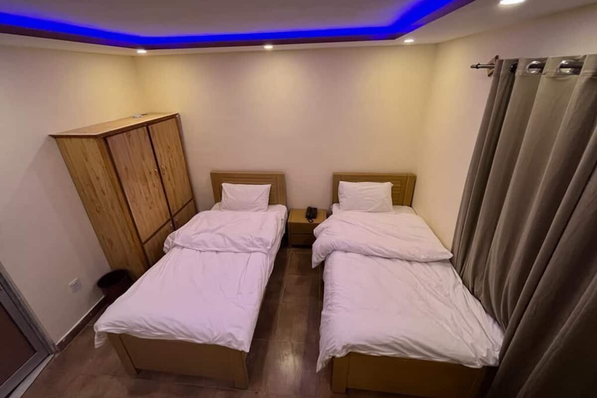 Una habitación con dos camas, un armario de madera, una mesita de noche y una cortina.