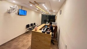 A conference room with a wooden desk, multiple chairs, a large fan, a television, and a glass partition. - Eden Rock Skardu (Skardu)