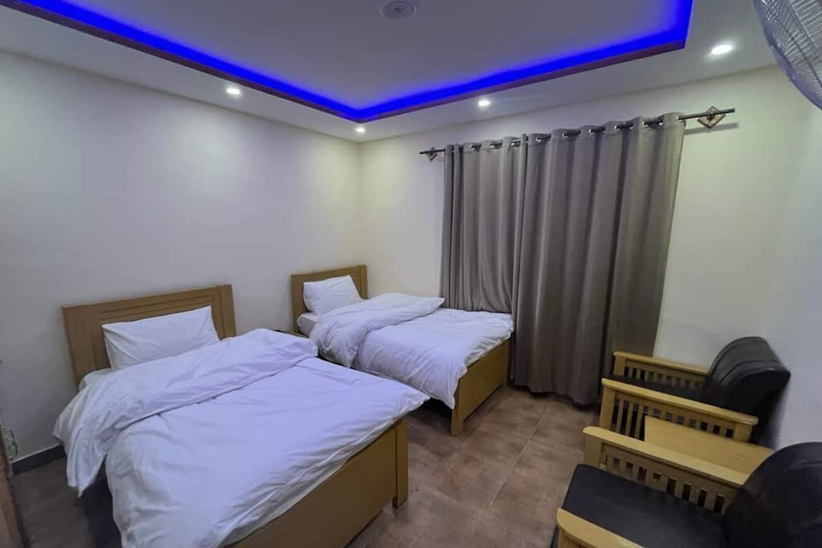 Una habitación de hotel con dos camas individuales, una zona de estar pequeña y un ventanal cubierto por cortinas.