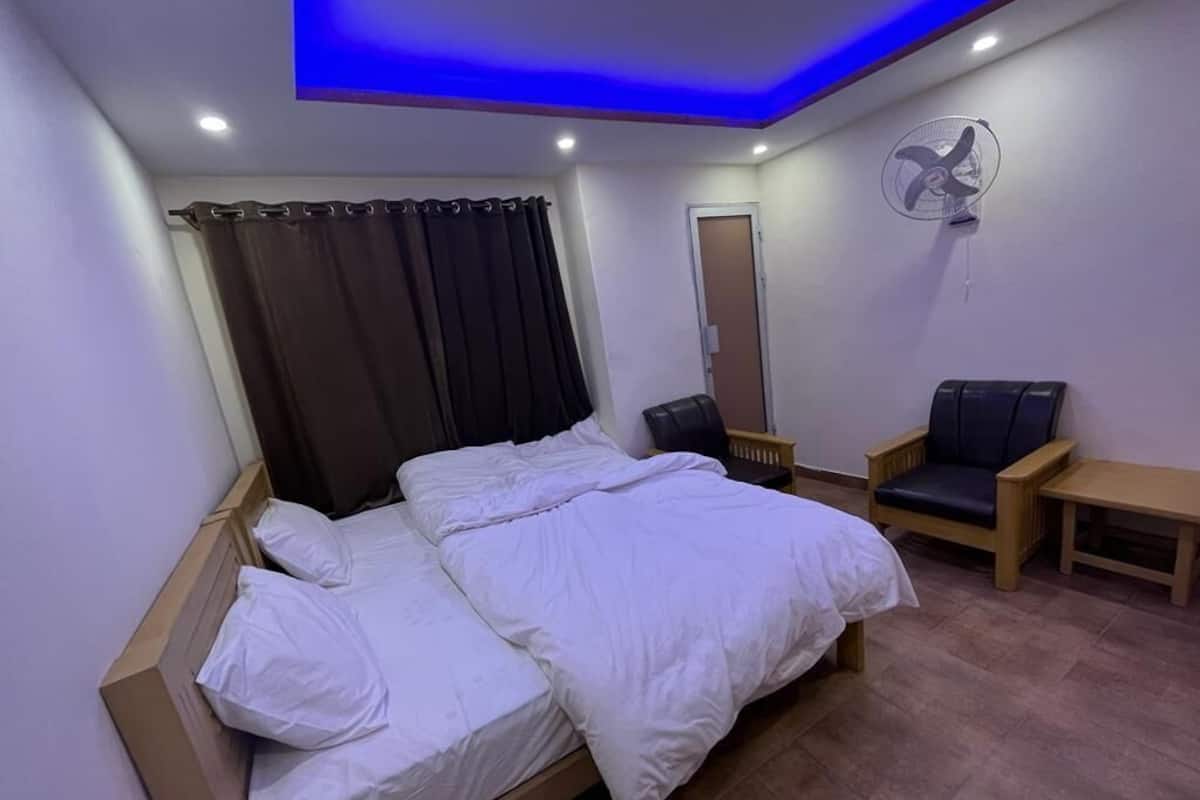 Un dormitorio con cama, una silla, una mesita, un ventilador y una puerta.
