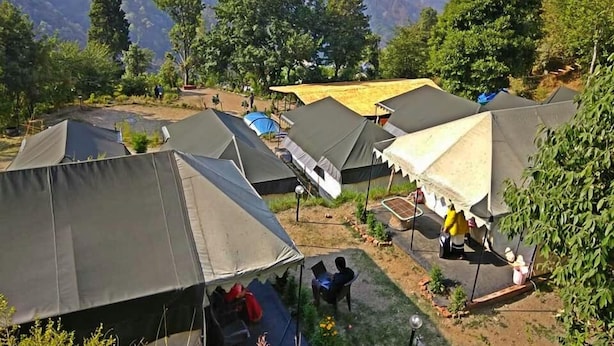 A campsite with multiple tents, some with attached awnings, set against a backdrop of mountains and greenery. - Hidden Valley Camp (Nainital)