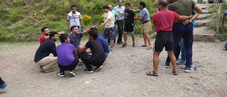 A group of people gathered outdoors, some sitting and others standing, with tents and houses in the background.