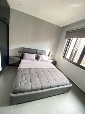 Un dormitorio moderno con una cama grande, una mesita de noche, un aparador y una ventana con persianas.