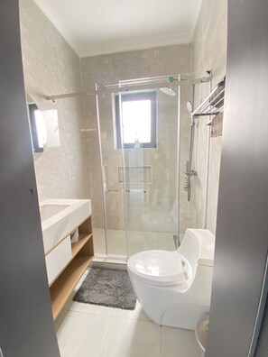 Un baño moderno con ducha envuelta en vidrio, inodoro blanco y tocador con espejo.