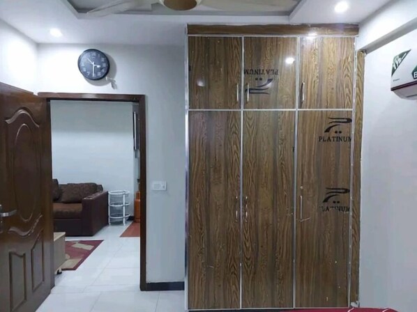 A hallway with a wooden wardrobe, a clock, and a sofa in the background. - Platinum Apartments (Lahore)