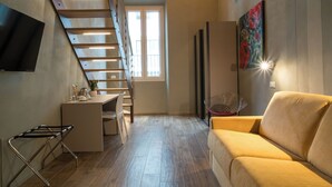 A modern living room with a staircase, a sofa, a dining area, and a TV mounted on the wall. - Gogò Petit Hotel (Florence)