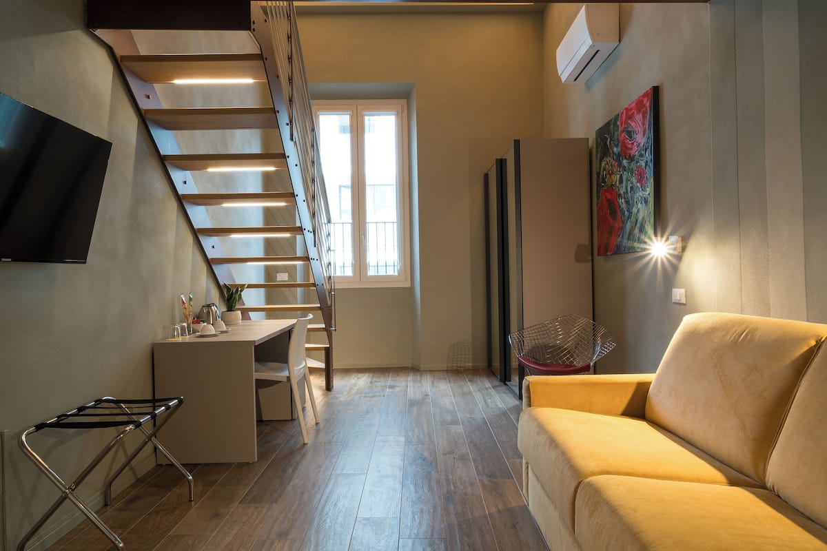 A modern living room with a staircase, a sofa, a dining area, and a TV mounted on the wall.