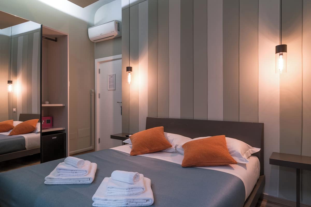 A hotel room with a bed, two nightstands, a mirror, and a wall-mounted air conditioner.