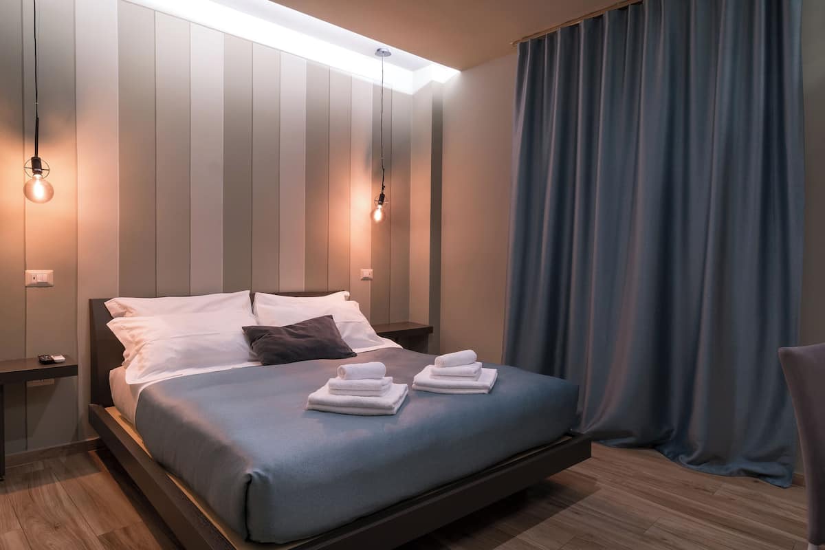 A modern hotel room with a large bed, two bedside tables, and a nightstand.