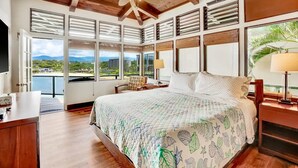 A spacious bedroom with a large bed, a desk, and a view of the outdoors. - Direct Oceanfront Kalapaki Beach Home, Wrap-Around Lanai, A/C, Views, Sleeps 8 (Lihue)