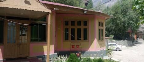 A single-story building with a sloped roof, a front porch, and a small garden area with flowers.