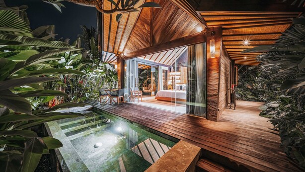 A modern house with a wooden deck, a swimming pool, and lush tropical plants. - Desa Hay Canggu (Tumbak Bayuh)