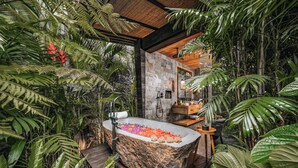 A naturalistic bathroom with a stone bathtub surrounded by lush tropical plants. - Desa Hay Canggu (Tumbak Bayuh)