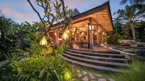 A modern outdoor lounge area with a pool, surrounded by lush greenery and a well-lit patio. - Desa Hay Canggu (Tumbak Bayuh)