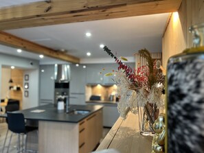 Uma cozinha moderna com vigas de madeira, uma ilha central e um vaso decorativo com plantas secas.