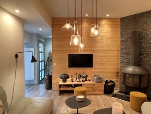 A modern living room with a fireplace, wooden panel walls, a flat-screen TV, and a variety of seating options. - [CheZ BlaisE]  (Cauterets)