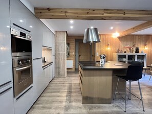 A modern kitchen with stainless steel appliances, a wooden ceiling, and a central island with bar stools. - [CheZ BlaisE]  (Cauterets)