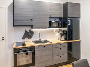 A compact kitchen with a microwave, coffee maker, oven, and a sink.