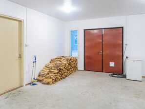 Een kamer met een stapelhout, een bezem, een deur en een koelkast.