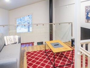 Sala de estar com sofá, mesa de centro, tapete vermelho estampado e janela com vista para árvores.