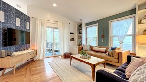 Ein modernes Wohnzimmer mit einem Flachbildfernseher, Holzboden, einer Couch, einem Couchtisch und einer Glastür zum Außenbereich.