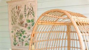Ein Korbstuhl mit weißen Kissen, ein kleiner Tisch mit einer Pflanze und eine botanische Illustration an der Wand.