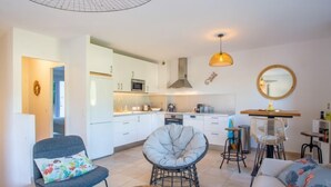 Ein modernes Wohnzimmer mit einer Couch, Sesseln, einem Couchtisch und einer Küchenzeile mit Schränken und Geräten.