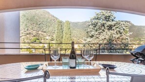 Ein runder Tisch mit einer Weinflasche, zwei Weingläsern und einer Wasserkaraffe auf einem Balkon mit Blick auf eine Berglandschaft.